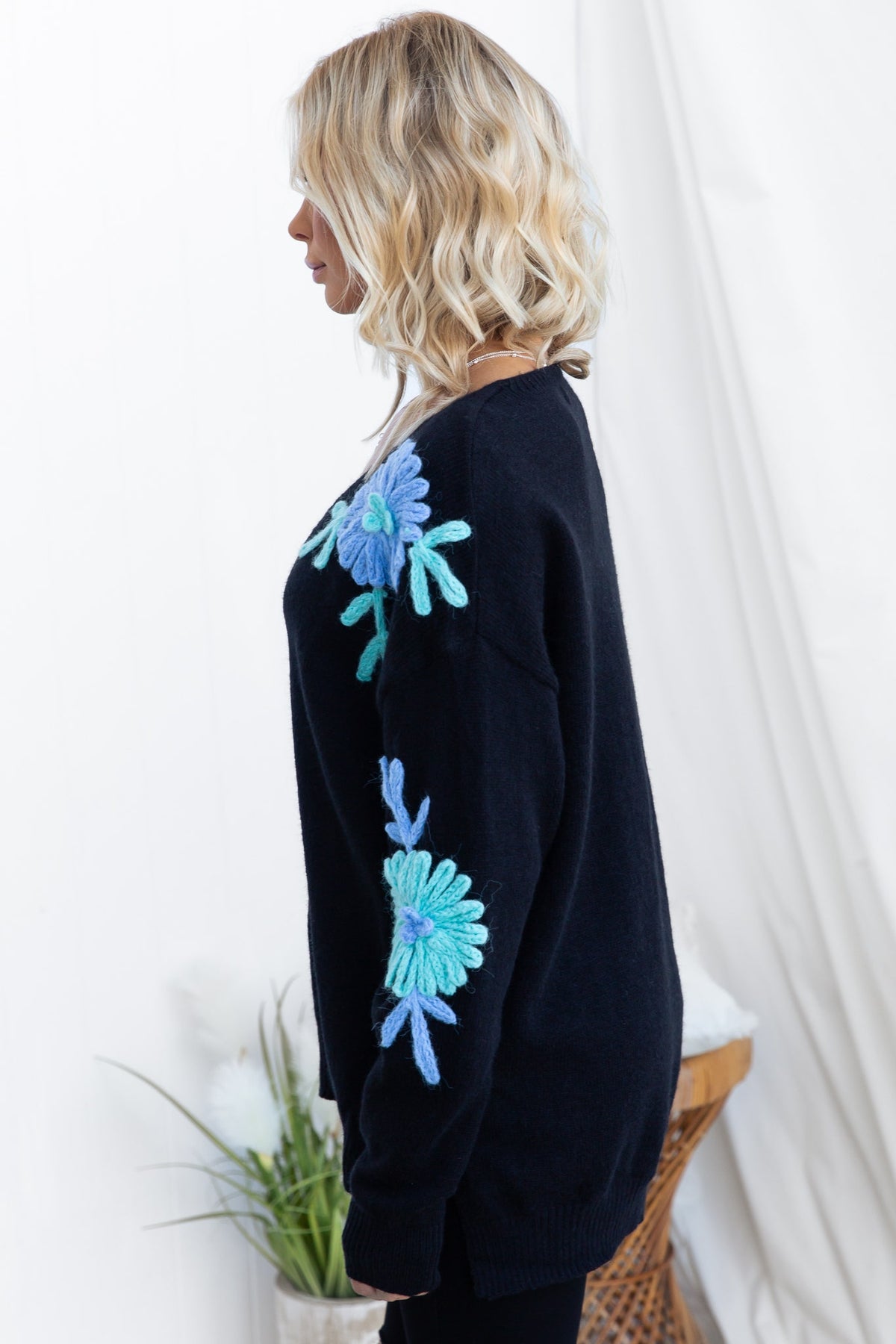 Side view of a model wearing a black knit Capa jumper with colorful floral embroidery, showcasing relaxed fit and stylish design.