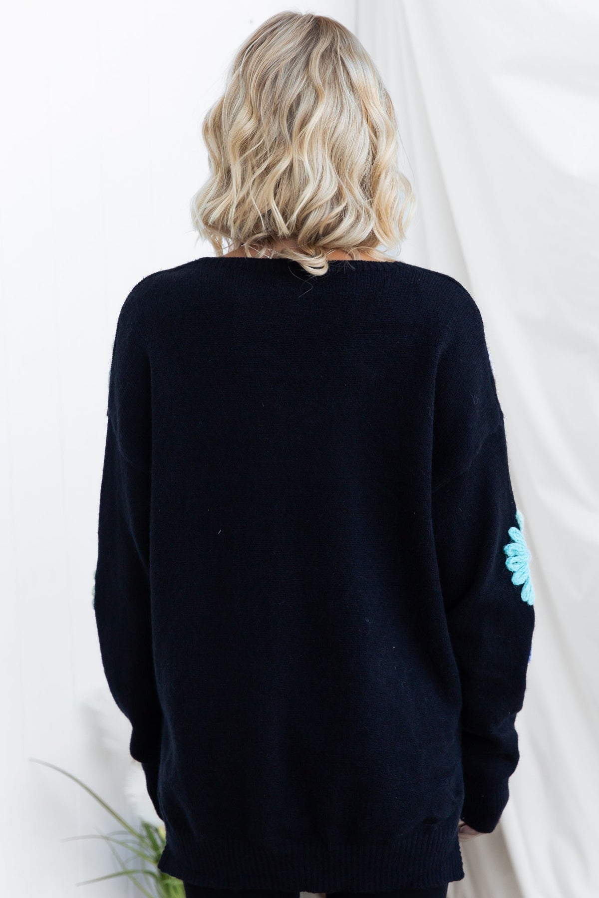 Back view of a black Capa Jumper with a relaxed fit and floral detail on sleeve.