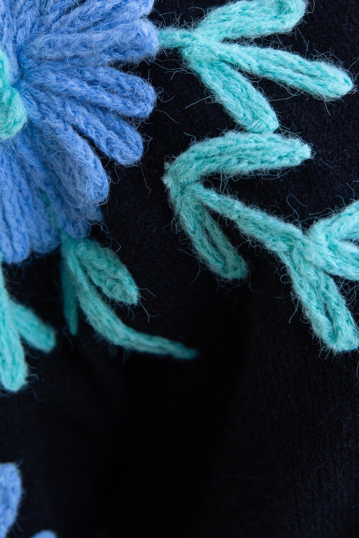 Close-up of black jumper showcasing blue flower and green leaf knitted patterns, highlighting the knit material.