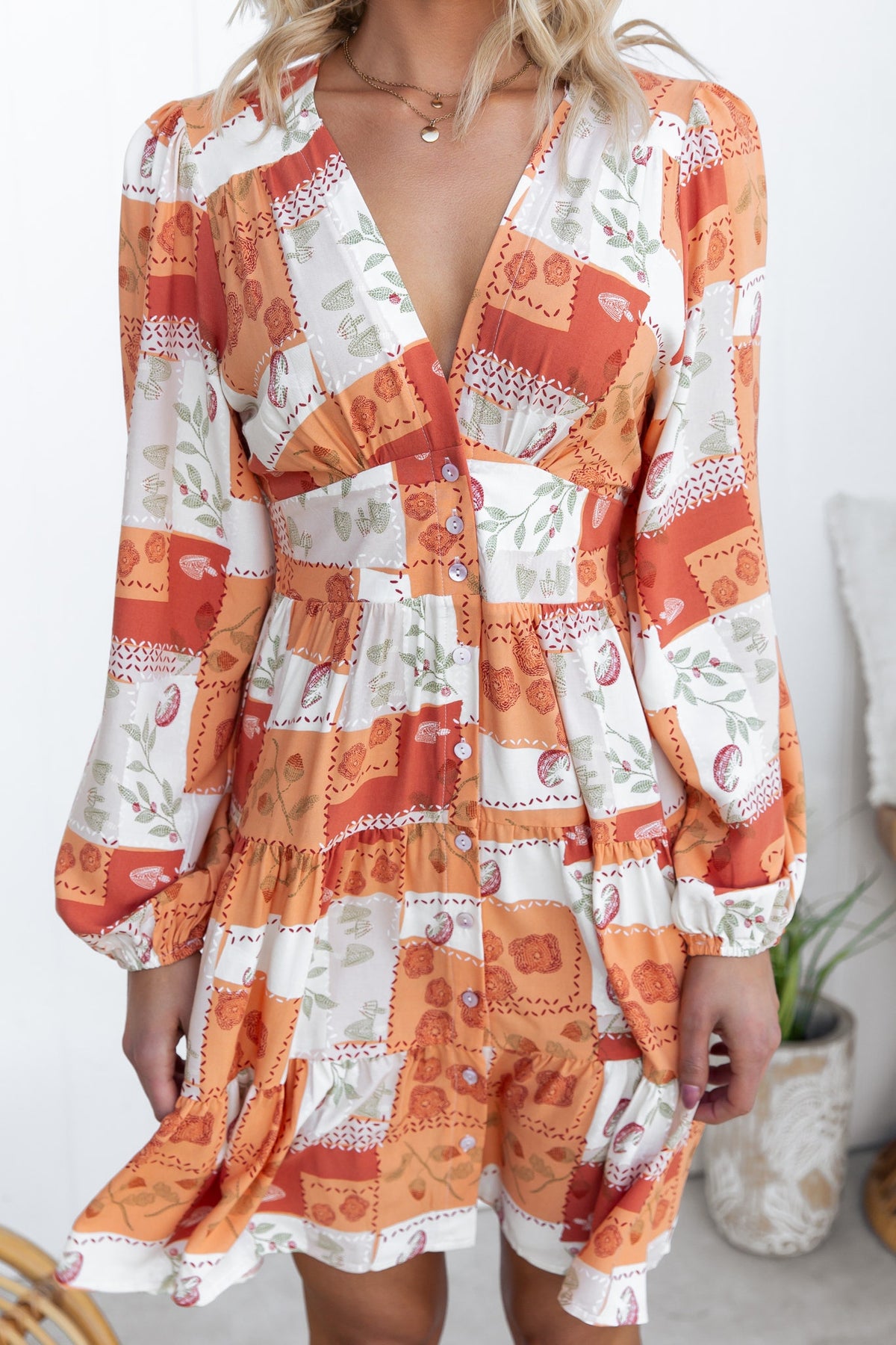 Coral dress with V-neckline, button-up front, and elastic cuffs, featuring stylish orange and white floral print.