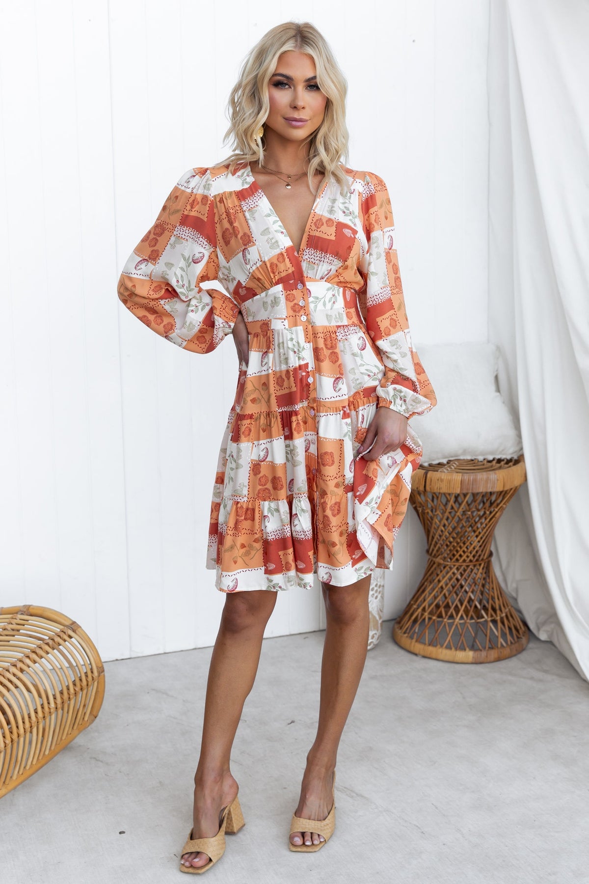 Model wearing a coral V-neck dress with button-up front and elastic cuffs, stylishly posed in a minimalistic setting.