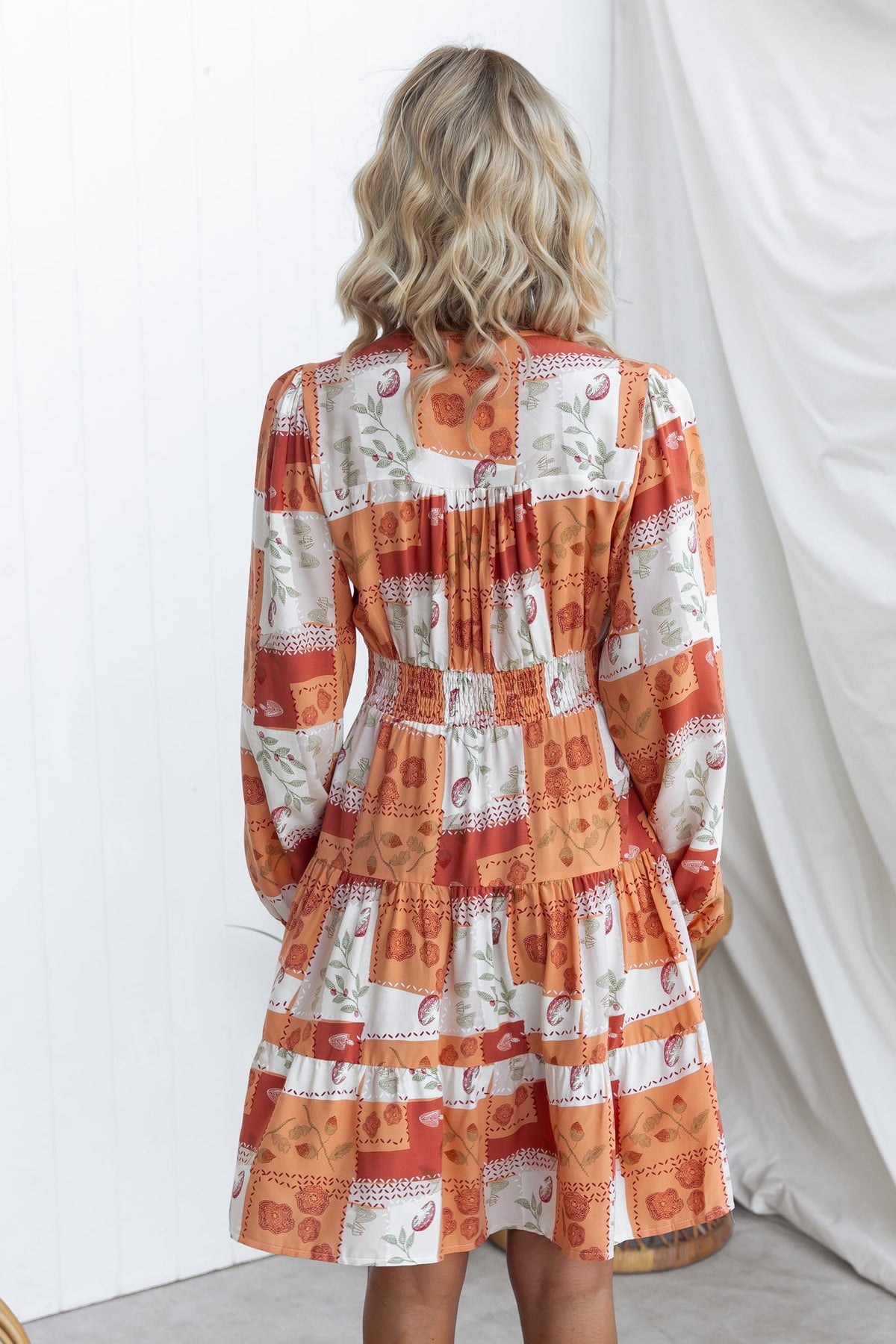 Back view of a coral dress with a V-neckline and button-up front, featuring elastic cuffs and a tiered skirt.