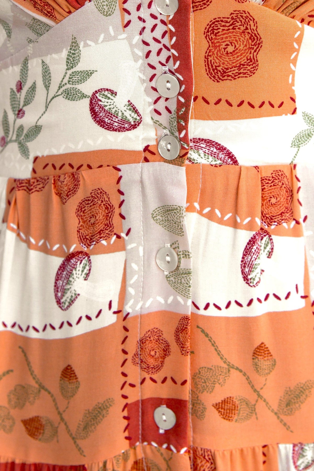 Close-up of a coral dress with floral patterns and a button-up front, featuring pockets and a V-neckline.