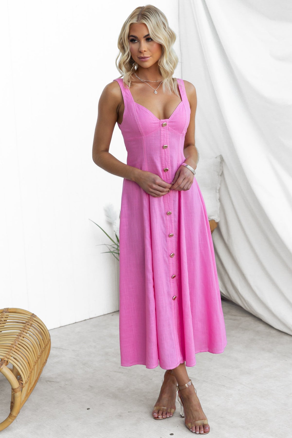 Model wearing a pink Lyre Midi Dress featuring faux buttons, elastic back, and lined bust, styled for a summer look.