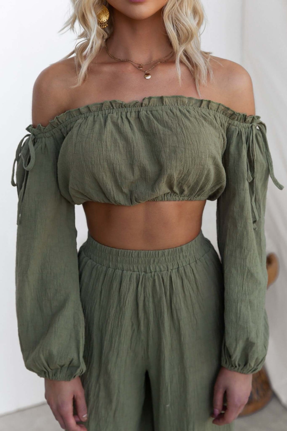 Olive green off-shoulder crop top with tie details and puff sleeves, styled with matching high-waisted pants.