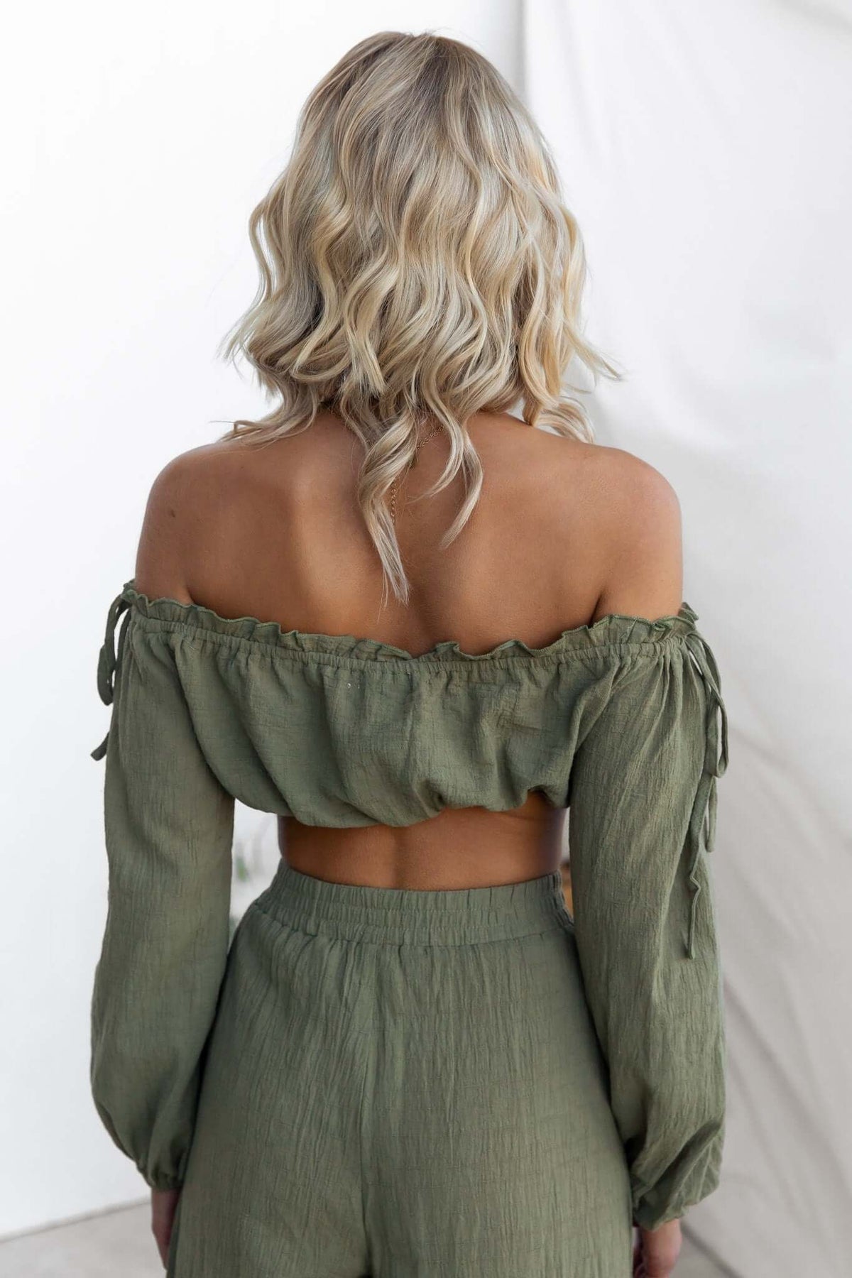 Back view of a woman in an olive green off-shoulder top with tie details, styled with matching bottoms.