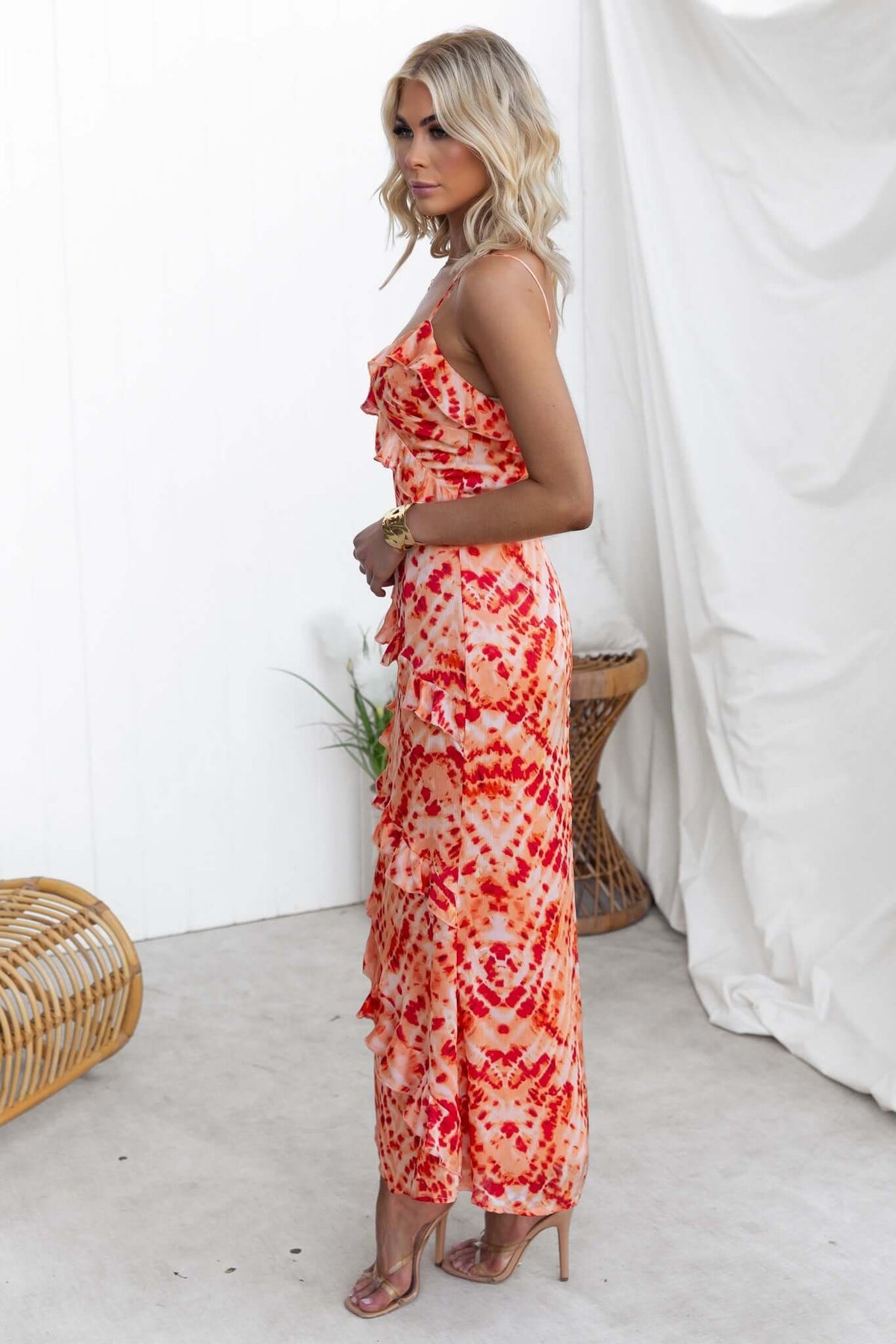 Model wearing an orange and red print Aquarius Maxi Dress with ruffle detailing and adjustable straps.