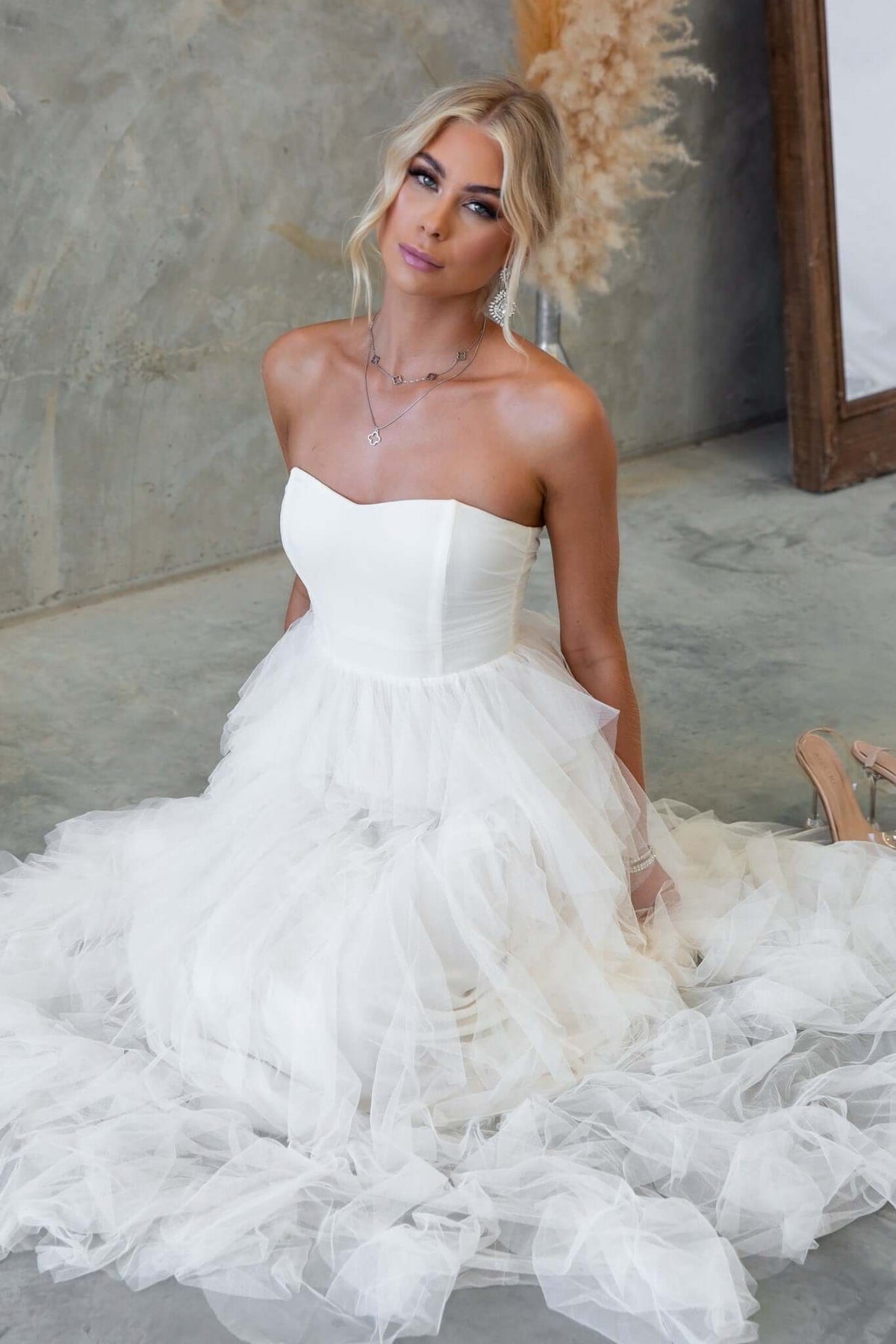 Carrie Maxi Dress in strapless design with tulle overlay and boning, styled in a modern indoor setting.