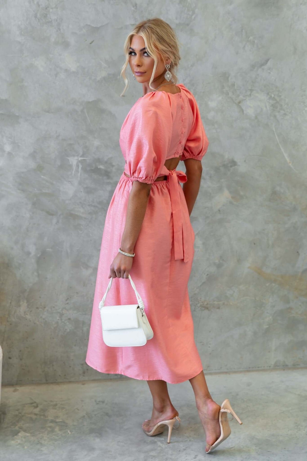 Model wearing an isabelline midi dress with puff sleeves and back cut-out, holding a white handbag.