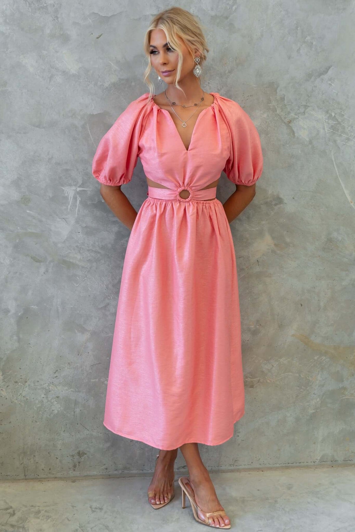 Isabelline midi dress in pink with puff sleeves, V-neckline, and waist button detail, worn by a model.