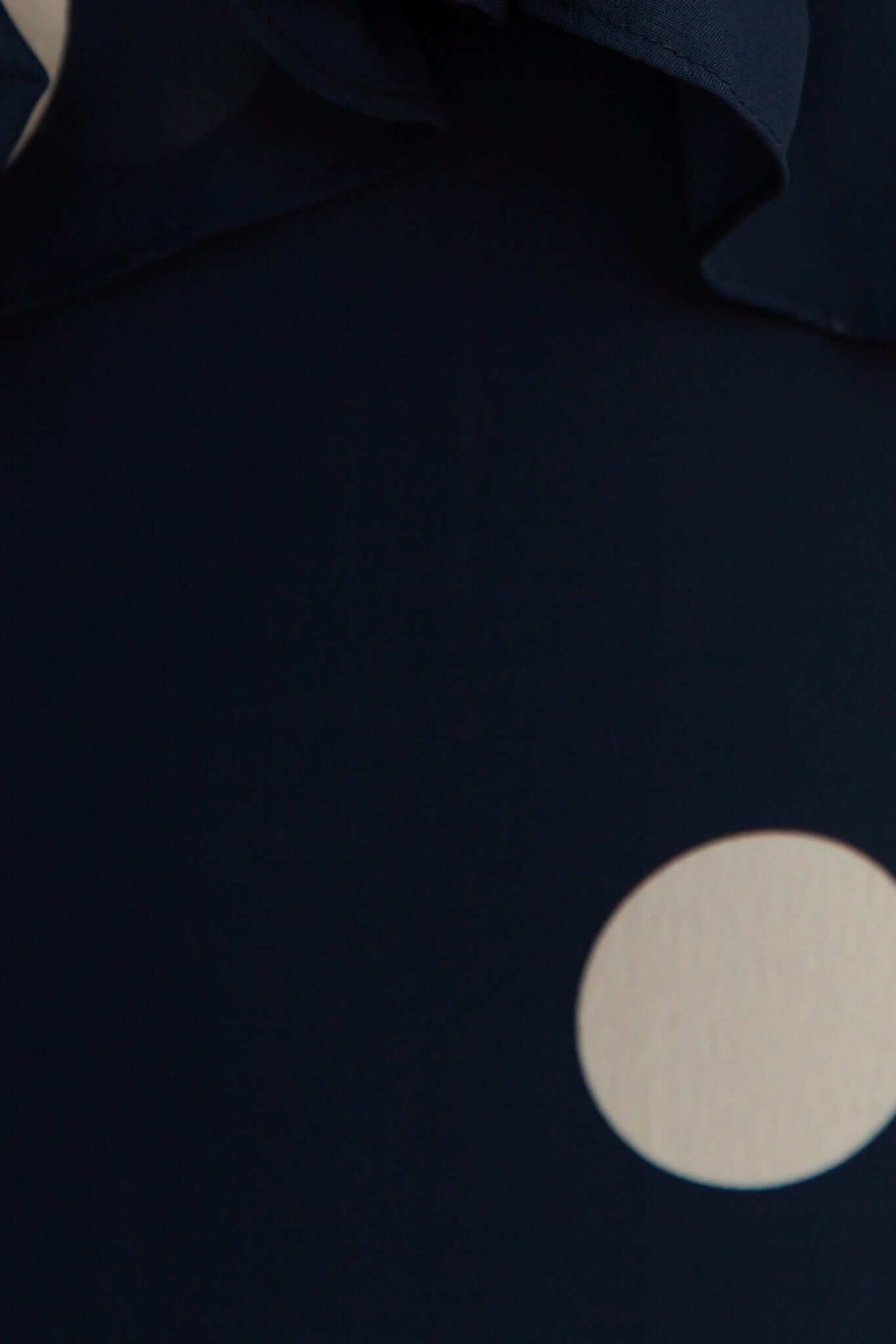 Close-up of navy fabric with a white polka dot pattern, featuring a ruffled detail.