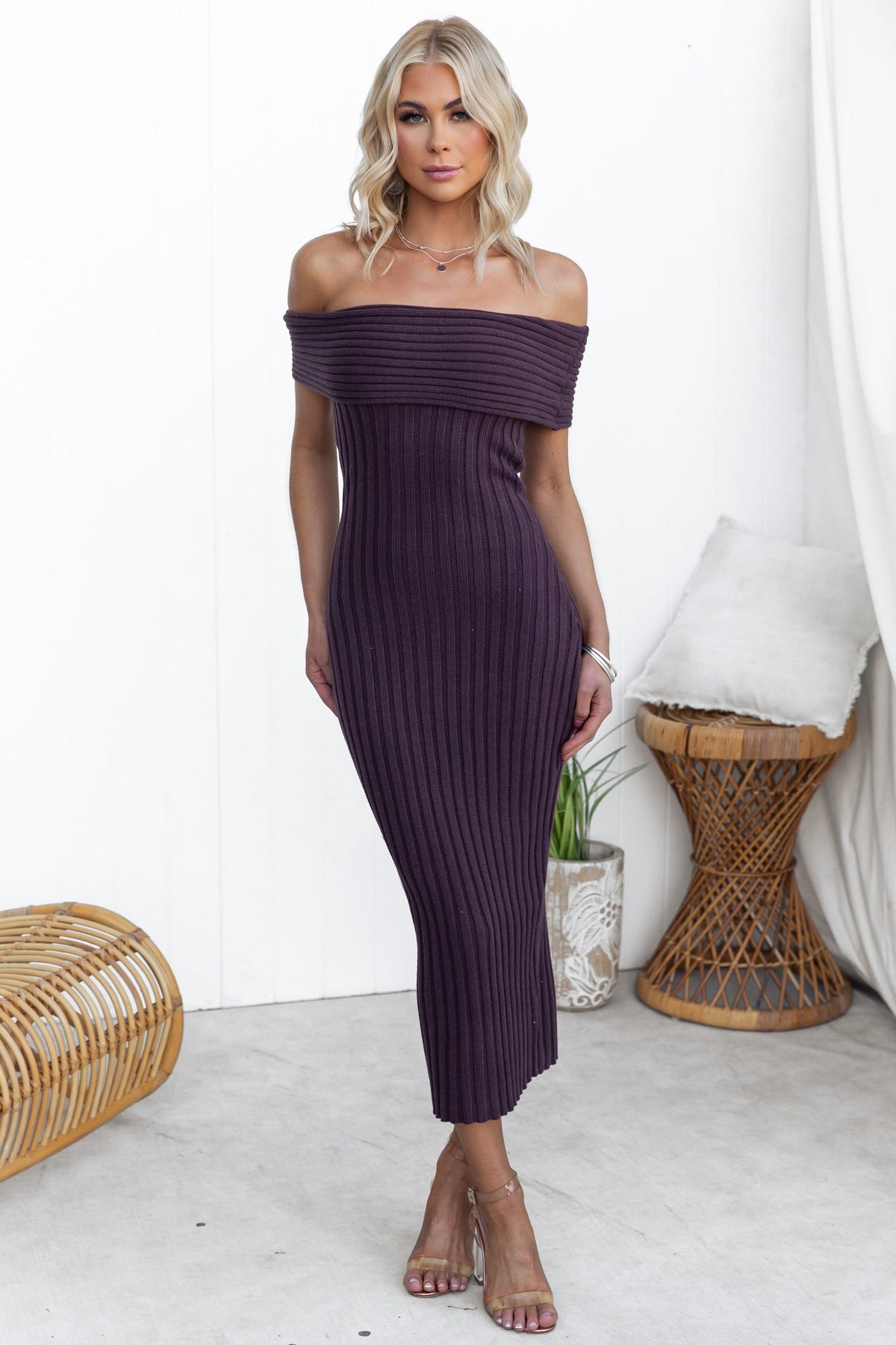 Model wearing a purple off-shoulder midi dress in ribbed knit material, showcasing a form-fitting style.