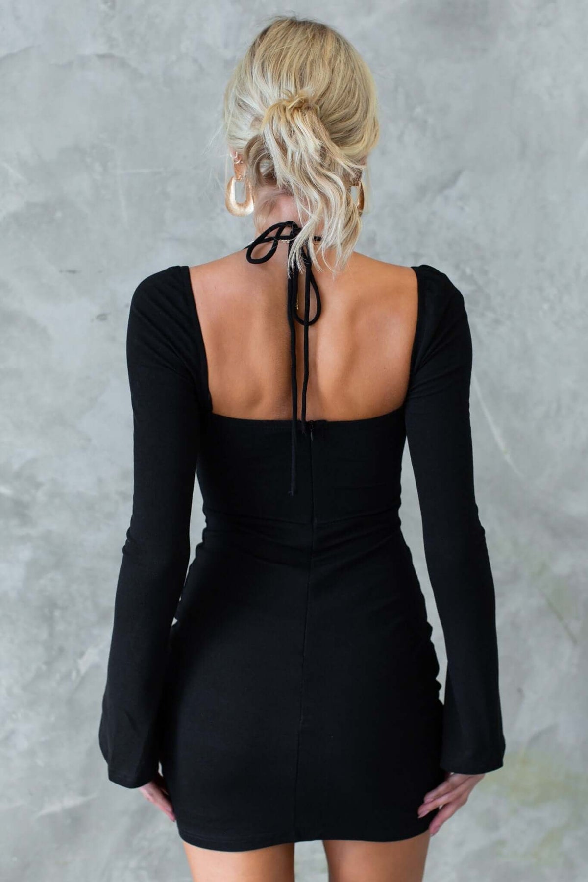 Back view of the Rehna Dress featuring a tie detail at neckline and long sleeves in black.