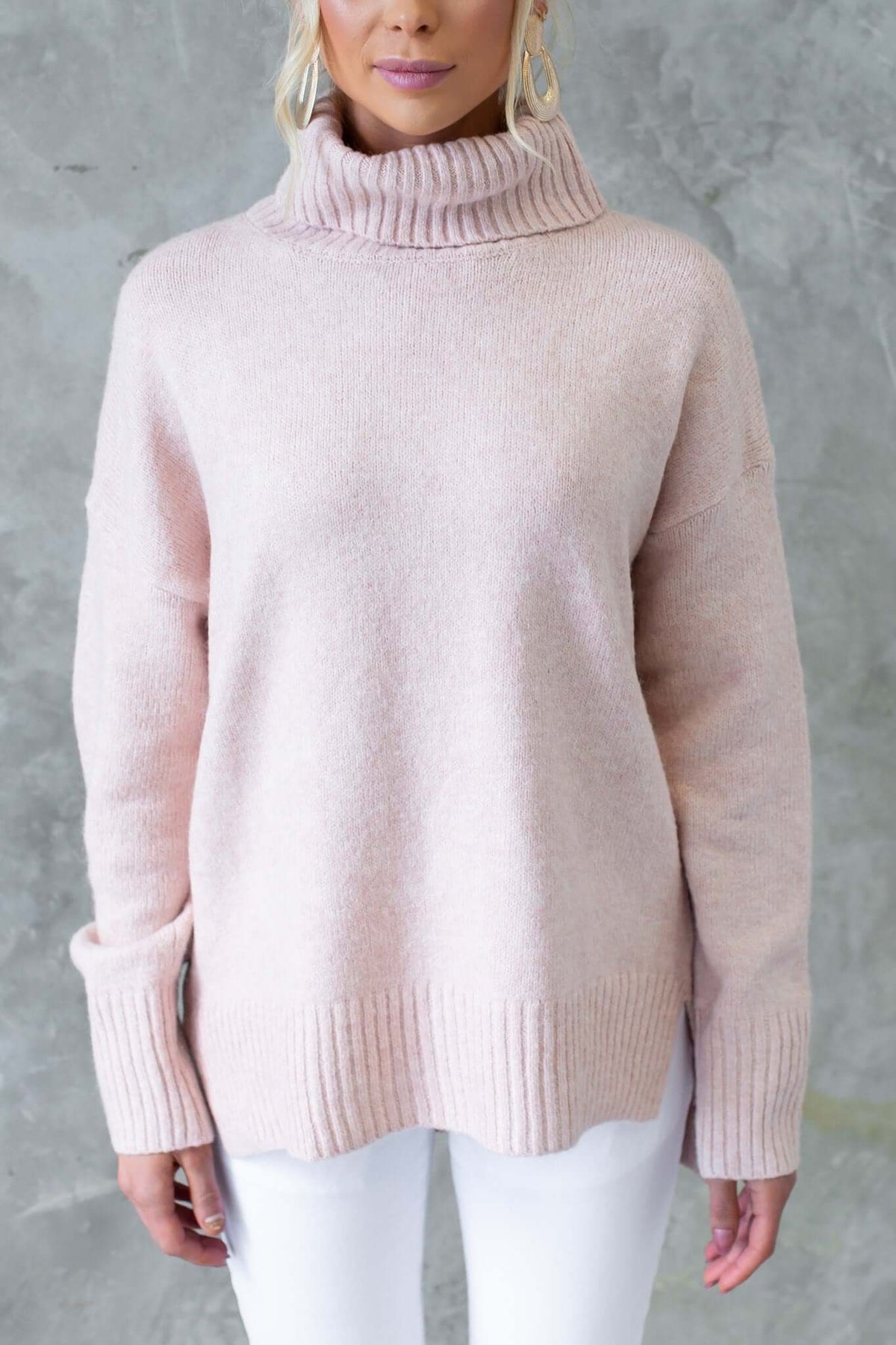 Light pink ribbed knit Orion jumper with turtle neckline and side splits, worn with white pants.