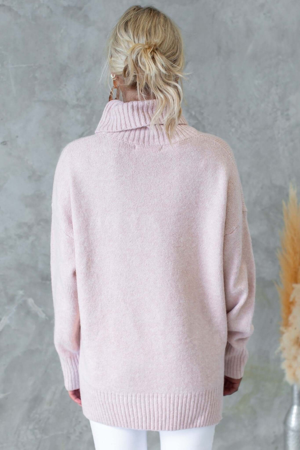 Back view of a ribbed pink Orion Jumper with turtle neckline and relaxed fit, styled with white pants.