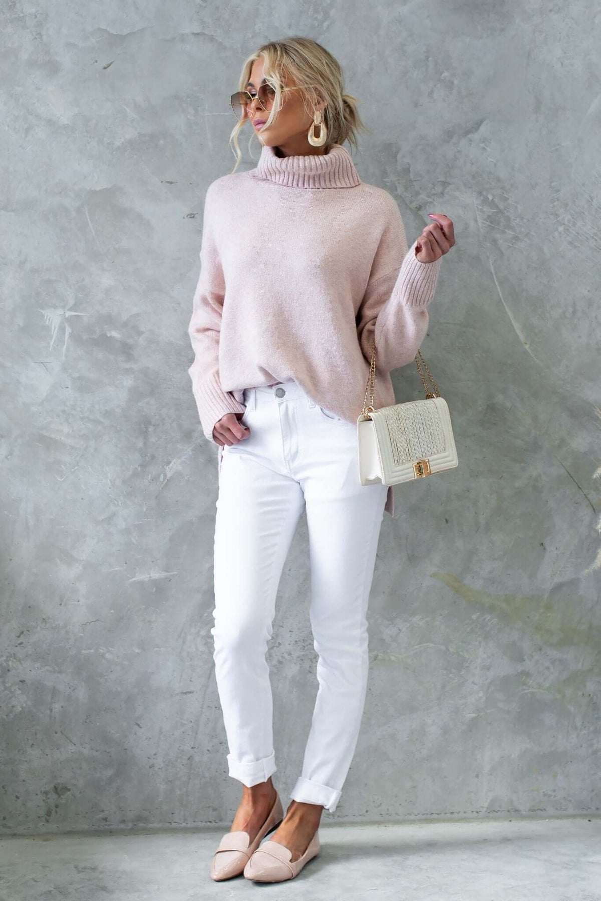 Model wearing a relaxed fit ribbed knit Orion Jumper in pink, paired with white jeans and stylish accessories.