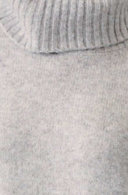 Close-up of a ribbed knit grey turtleneck jumper showcasing its soft texture and relaxed fit.