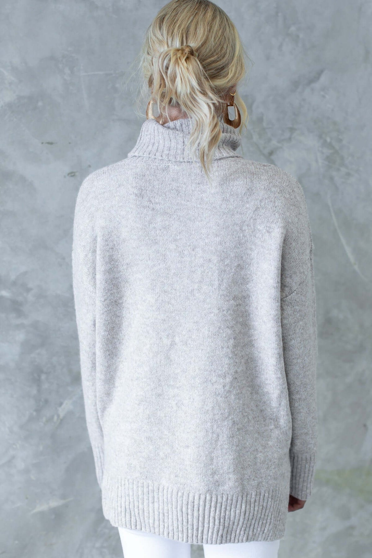 Back view of a light grey ribbed knit jumper with turtle neckline and small side splits, worn casually.