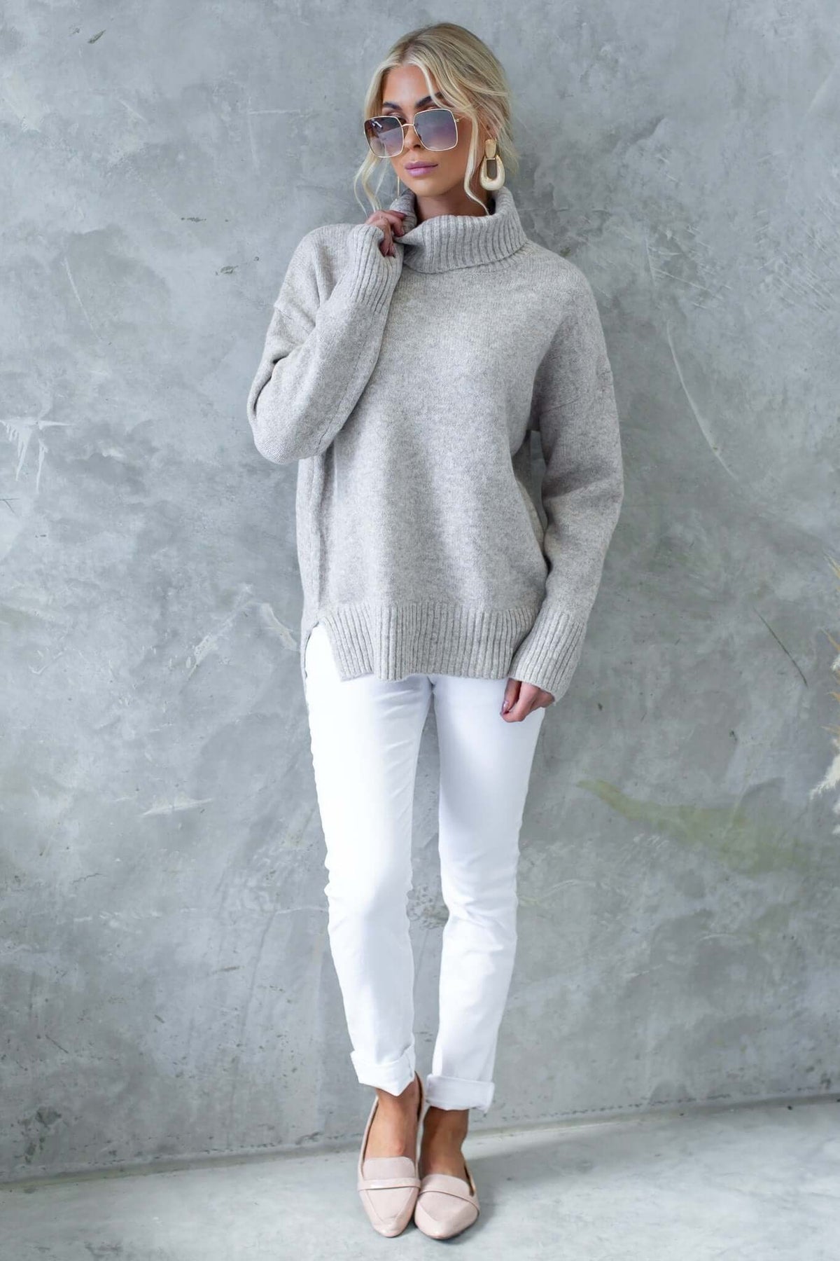 Model wearing Orion Jumper in light gray, featuring a turtle neckline and relaxed fit, paired with white pants.