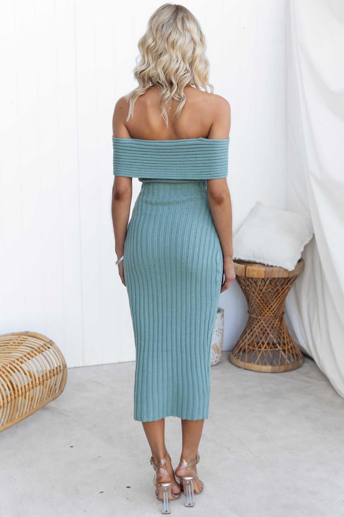 Back view of a woman in a teal ribbed midi dress with off-shoulder neckline, showcasing a fitted silhouette.