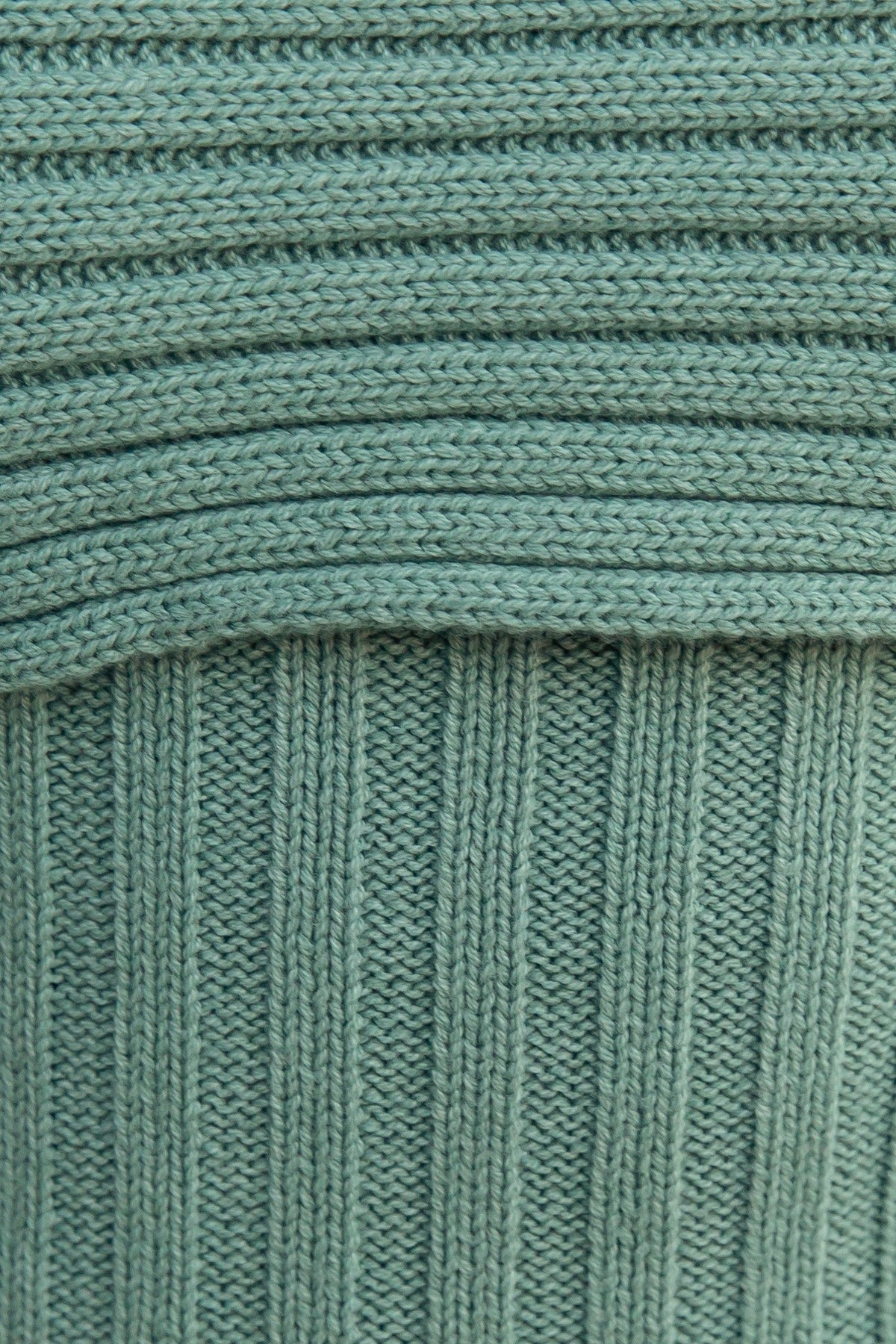 Close-up of ribbed knit fabric in soft green color, showcasing texture and pattern for a cozy, stylish look.