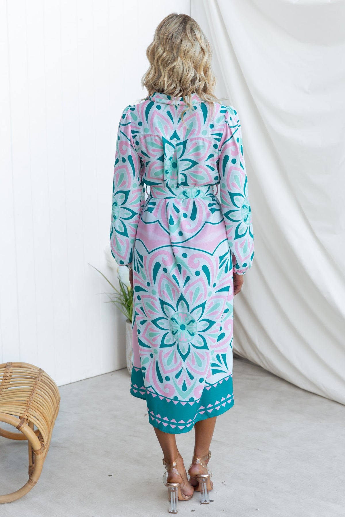 Back view of a model in the Faenza Midi Dress featuring floral patterns in teal and pink, styled with a woven chair.