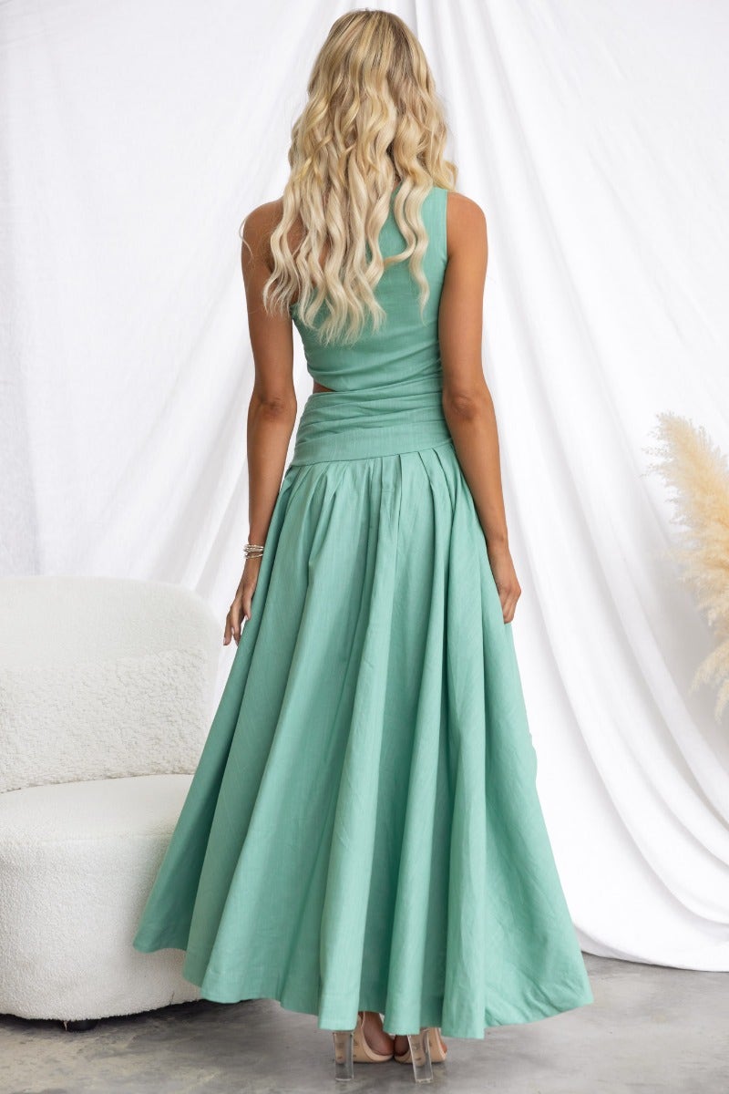 Back view of a woman wearing a mint green cotton blend maxi dress with a one-shoulder neckline and flowing skirt.