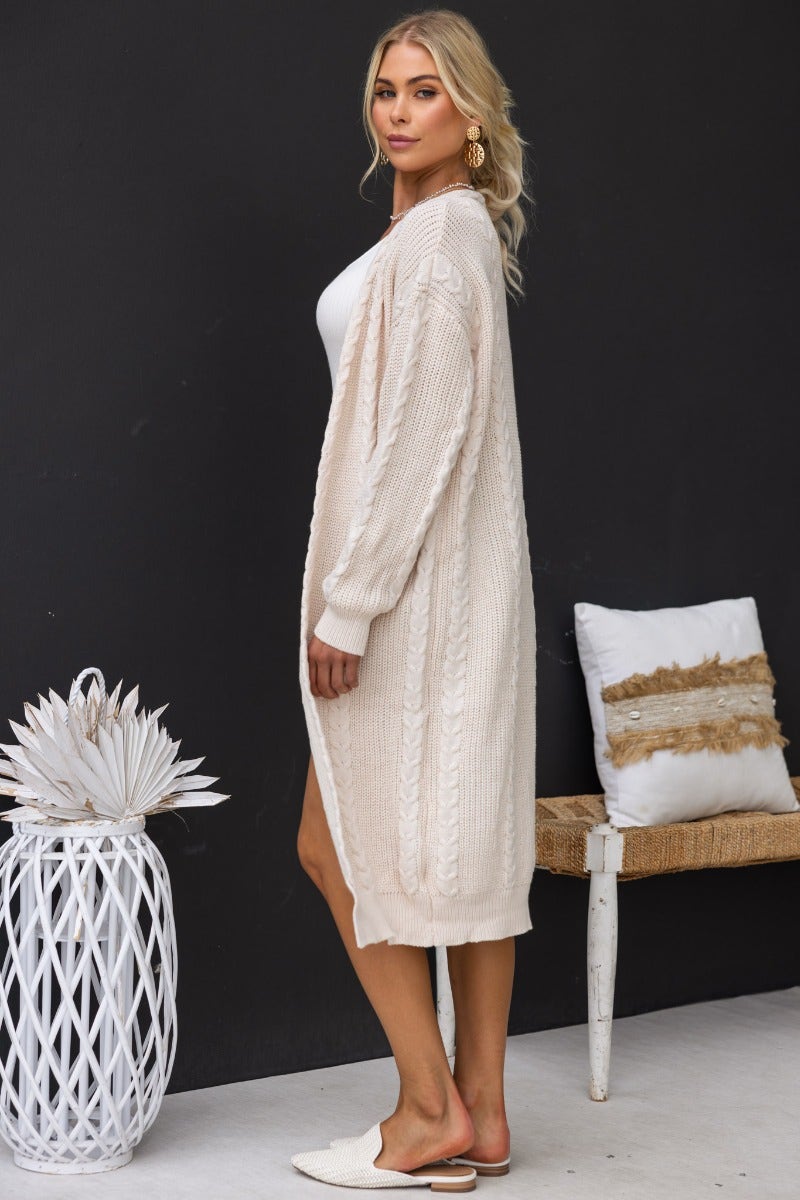 Longline cable knit Dwyn Cardigan in soft beige, styled with a white top, showcasing a relaxed fit and elegant design.