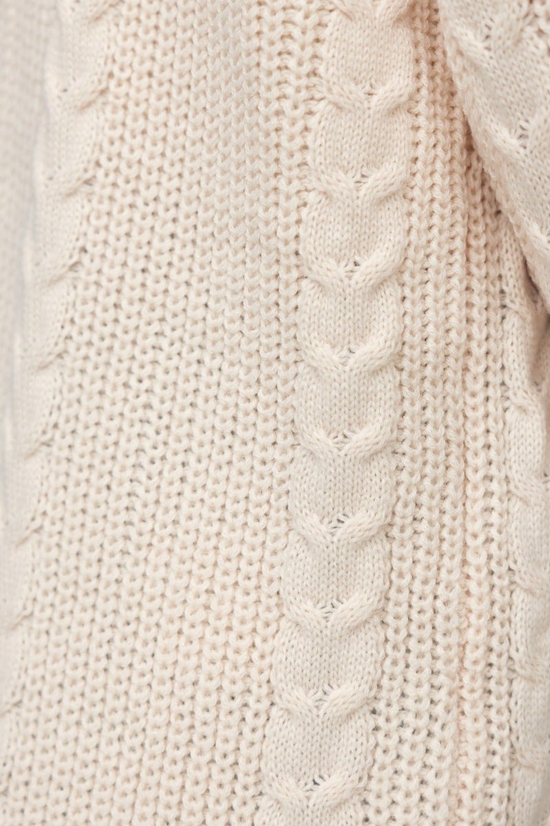 Close-up of Dwyn Cardigan showcasing intricate cable knit design in soft beige acrylic fabric.