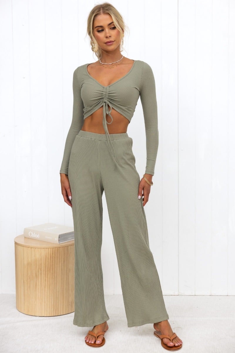 Model wearing Smitten pants in olive green, featuring a ribbed knit design and wide legs with an elastic waistband.