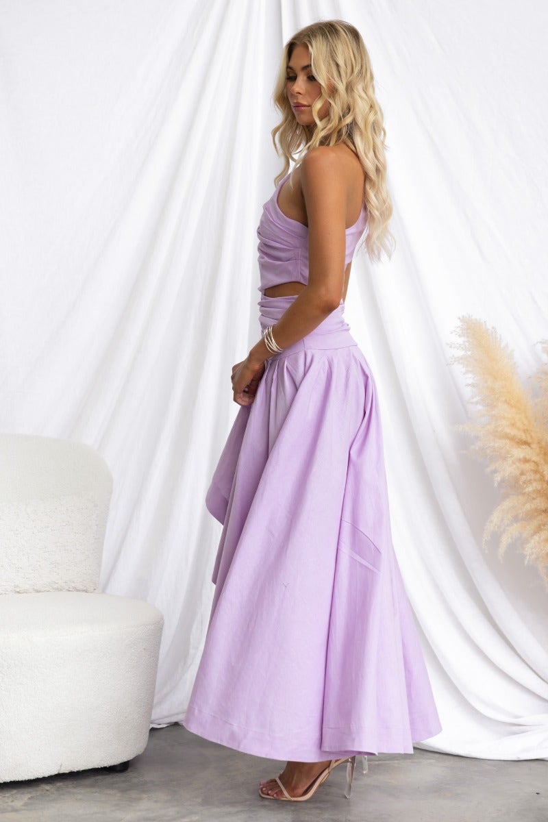 Model wearing a lavender Horizons Maxi Dress with one-shoulder neckline and asymmetrical hemline, styled in a soft setting.