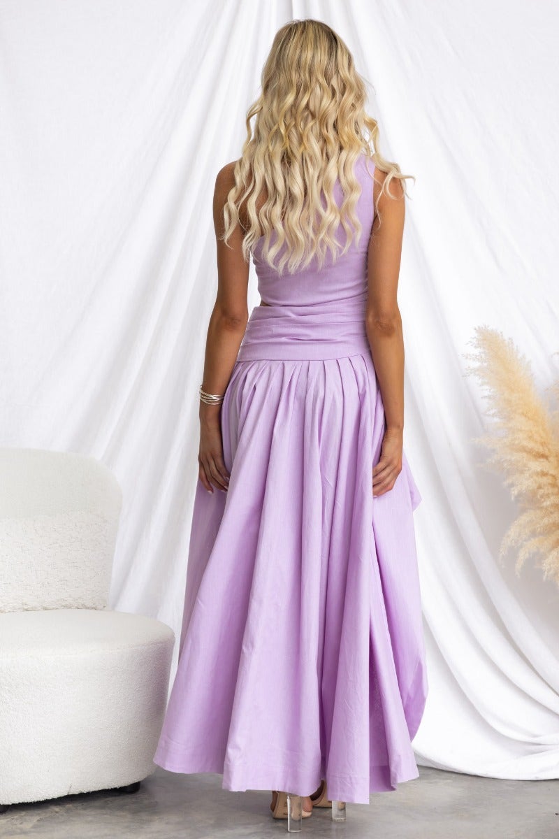 Back view of a model in a lavender Horizons Maxi Dress with one-shoulder design and flowing skirt.