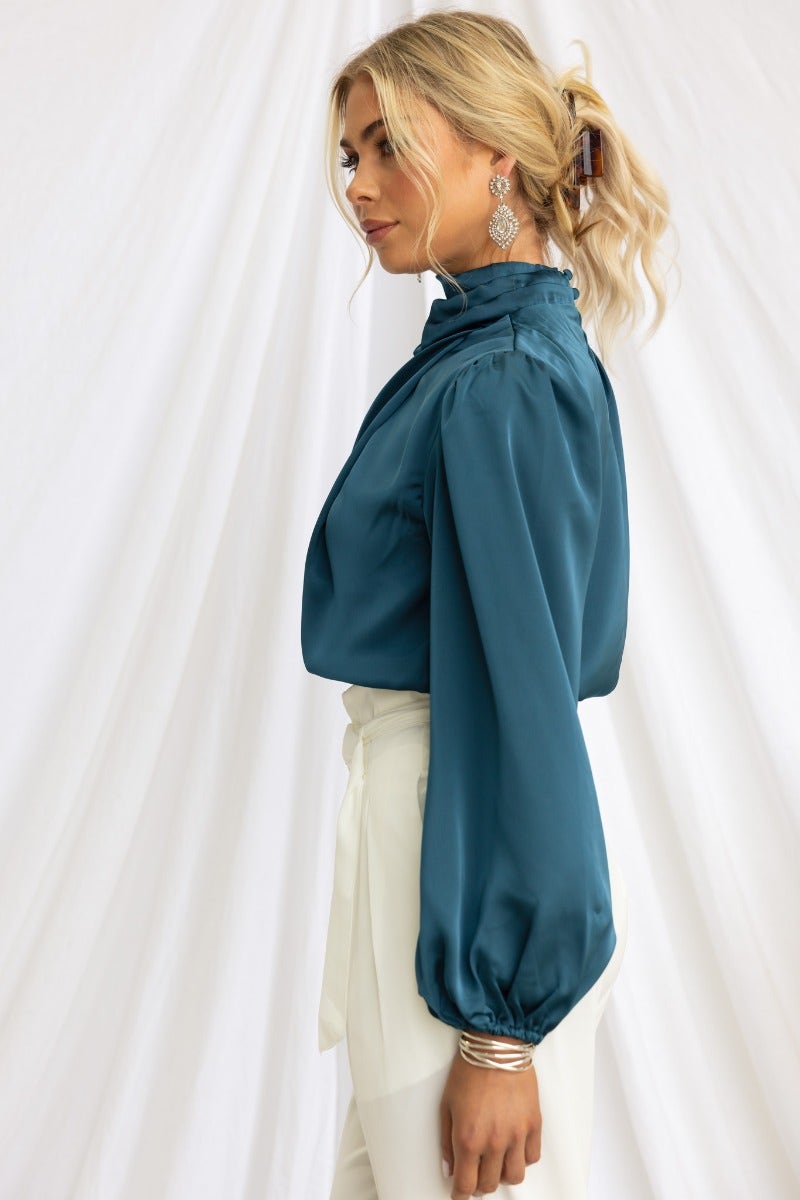 Elegant satin Xali top with high neckline, elastic cuffs, and buttons, styled with white pants.