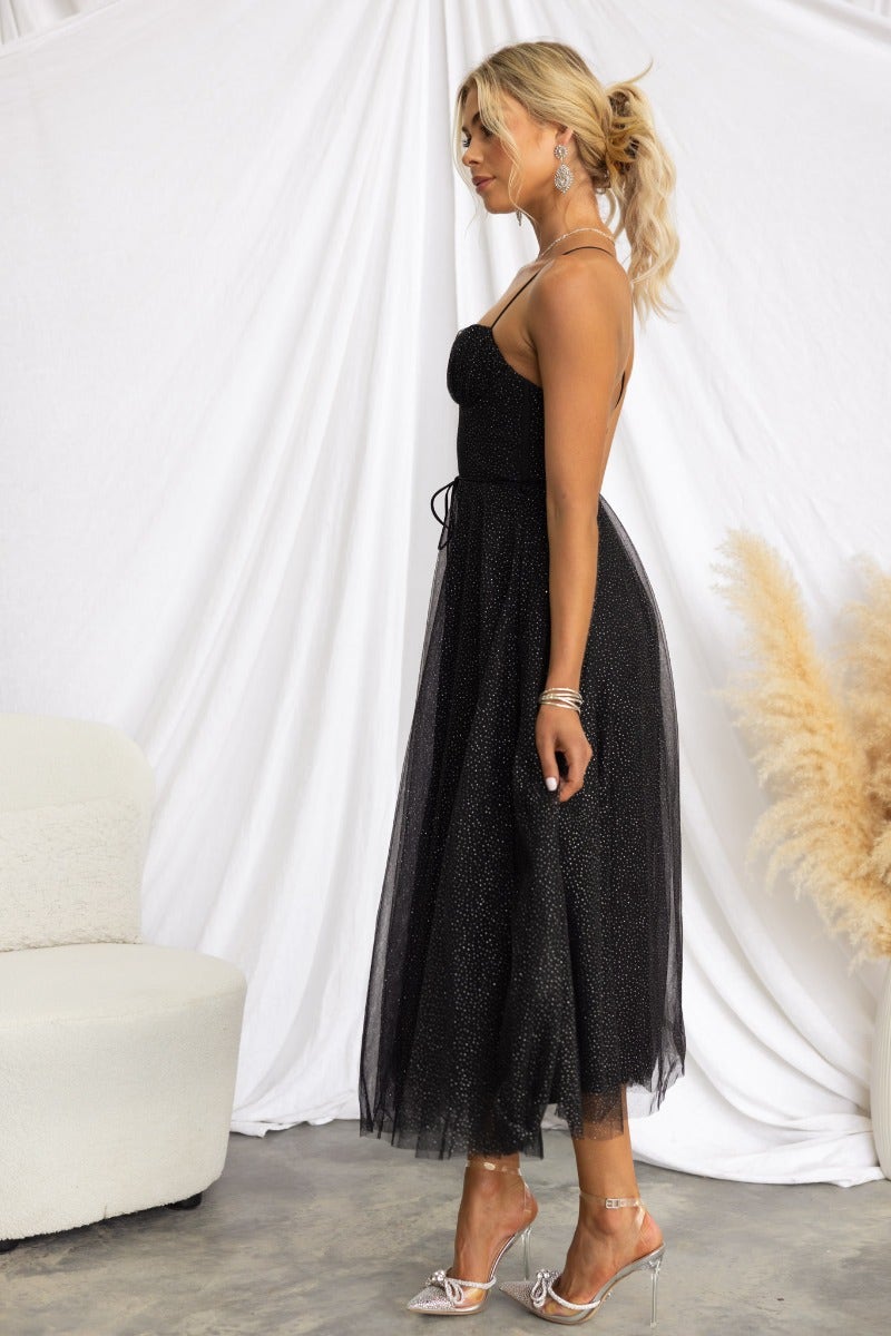 Model wearing a black tulle Florence midi dress with adjustable straps and glitter detail, styled with heels.