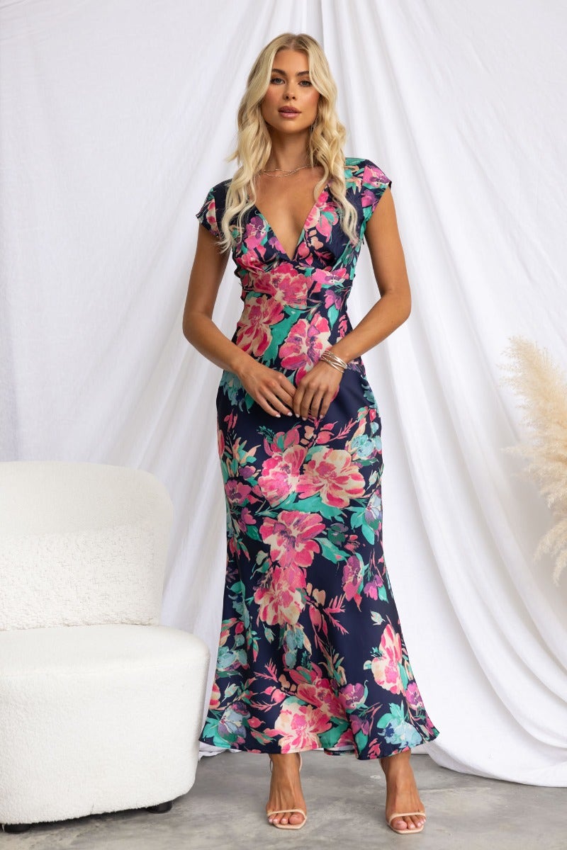Navy floral print maxi dress with V-neckline, cap sleeves, and twist detail at the back, styled with a clutch.