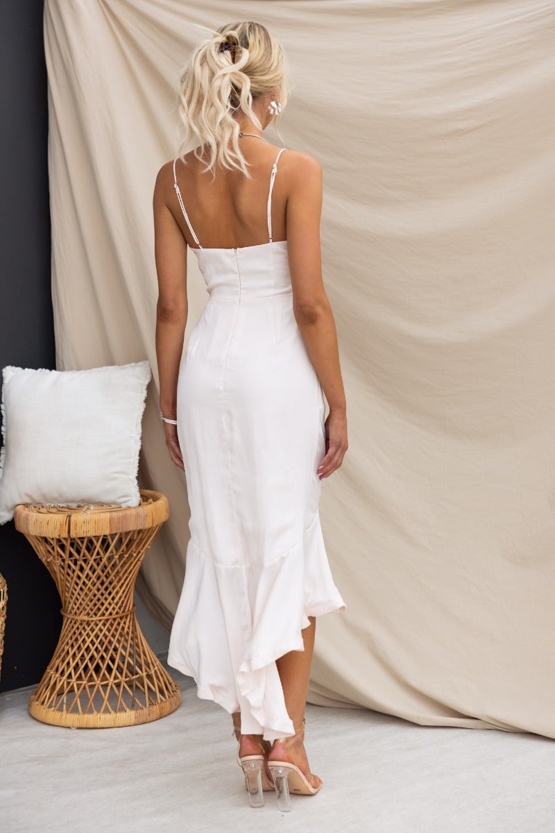 Back view of woman in Brooks Midi Dress with adjustable straps and frill hemline against a neutral backdrop.