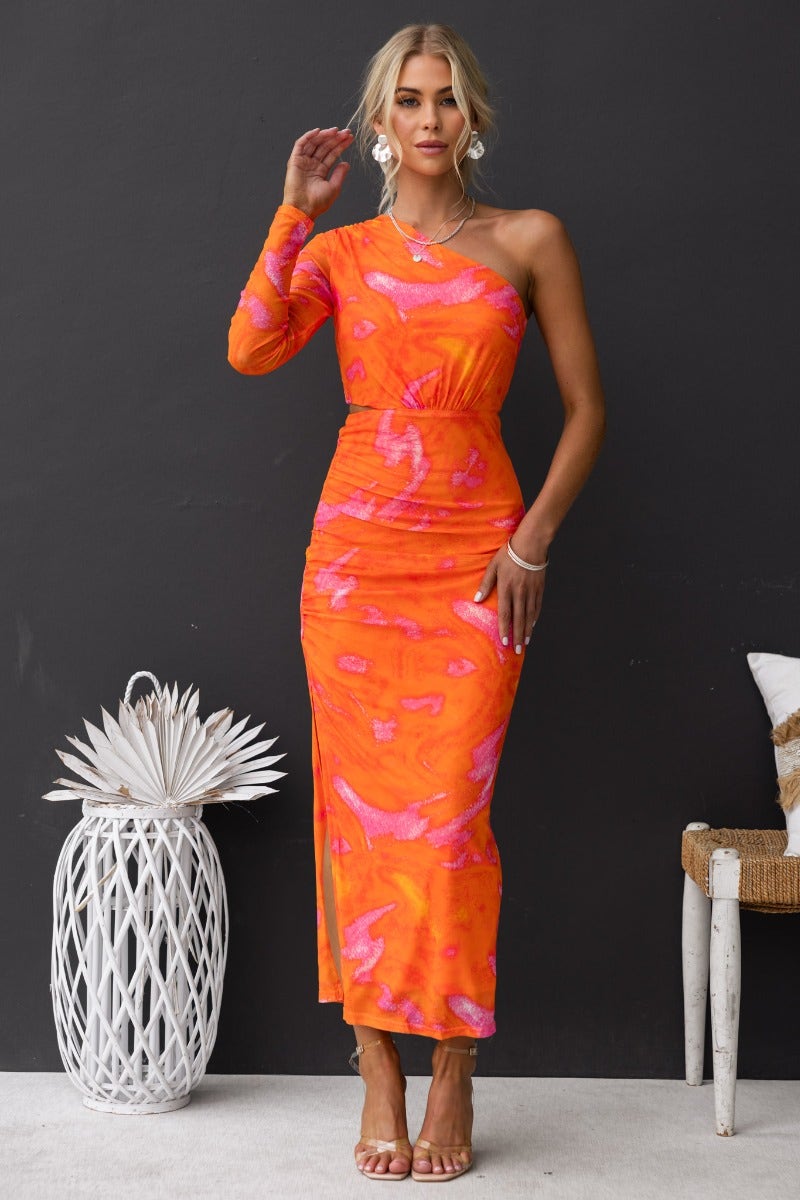 Model wearing a vibrant one-shoulder orange maxi dress with cut-out waist and side split, styled against a dark backdrop.
