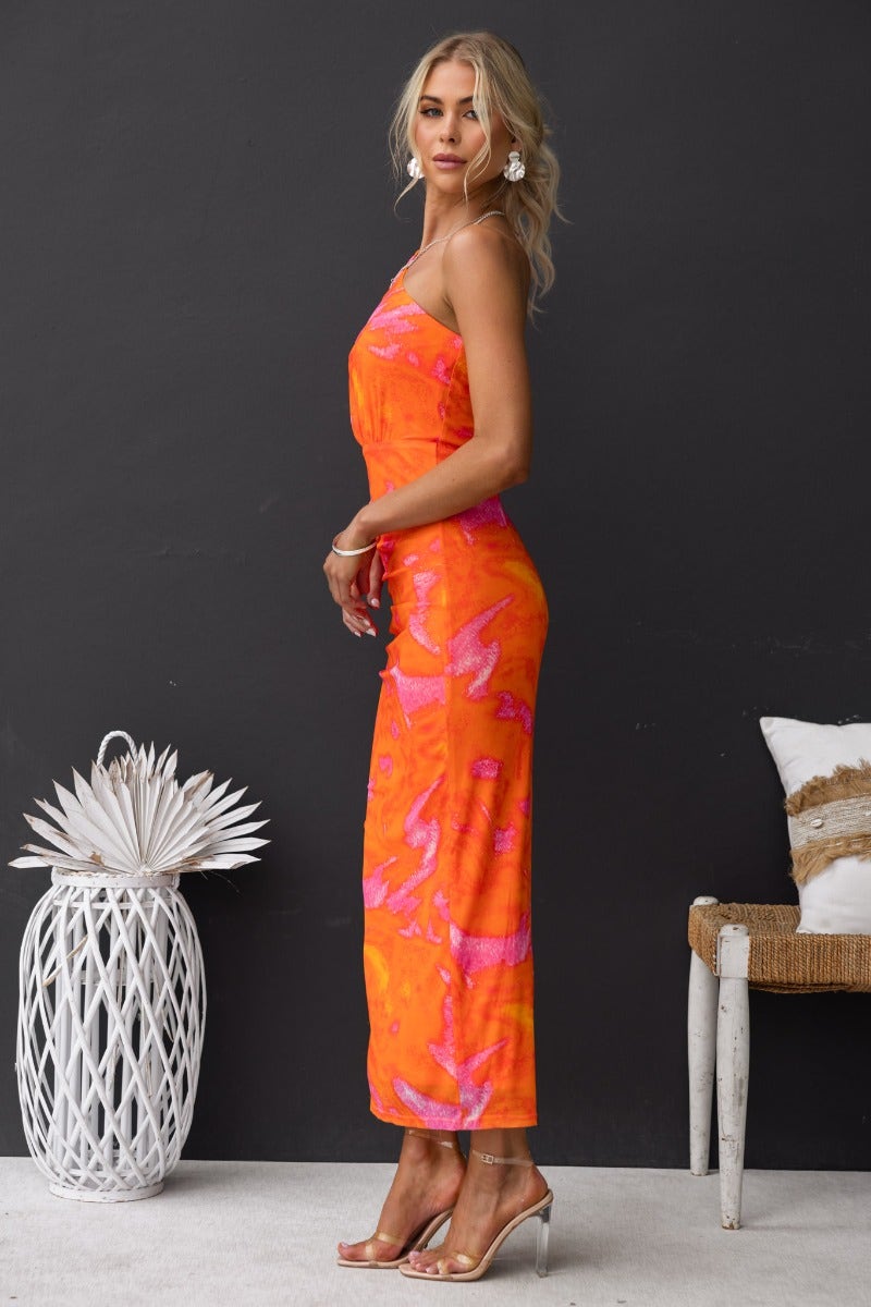 One-shoulder orange maxi dress with cut-out waist and side split, modeled against a dark background.