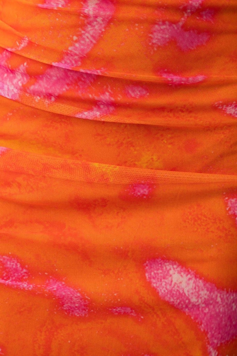 Close-up of vibrant orange fabric with pink abstract patterns, showcasing the texture and design of a maxi dress.