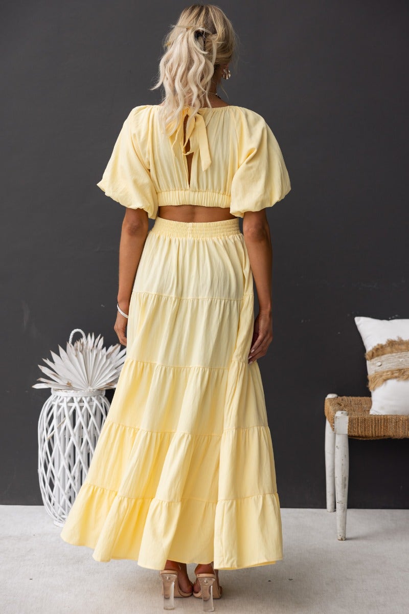 Back view of a woman in a yellow cotton Posh Maxi Dress with an off-shoulder neckline and tiered skirt.