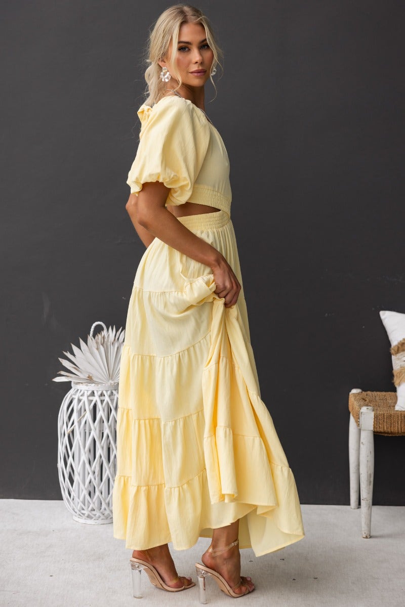 Posh maxi dress in soft yellow, featuring off-shoulder neckline, cut-out waist, and tiered skirt for summer outings.