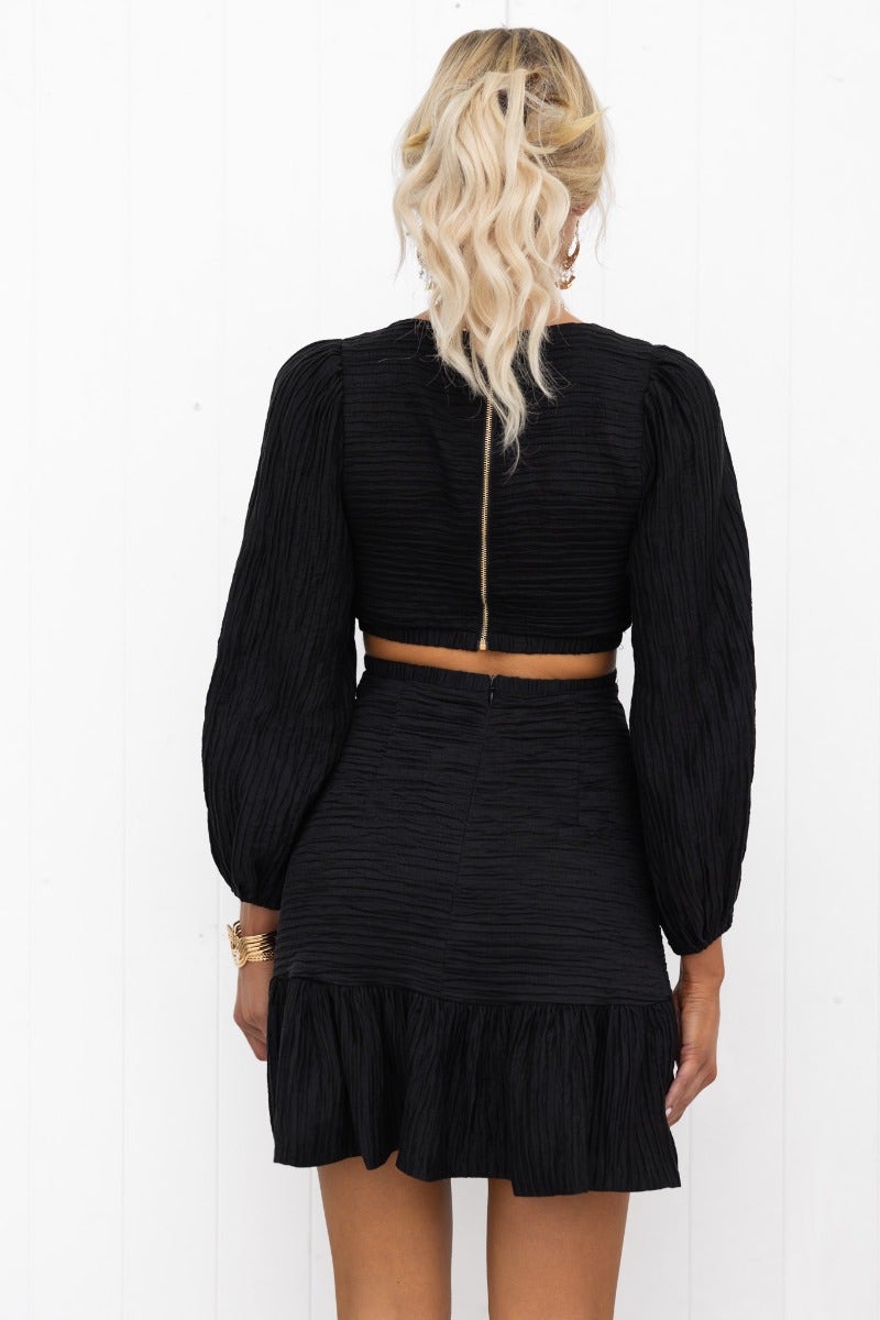 Back view of Tovia Dress featuring a textured black material, cut-out at waist, and puff sleeves with elastic cuffs.