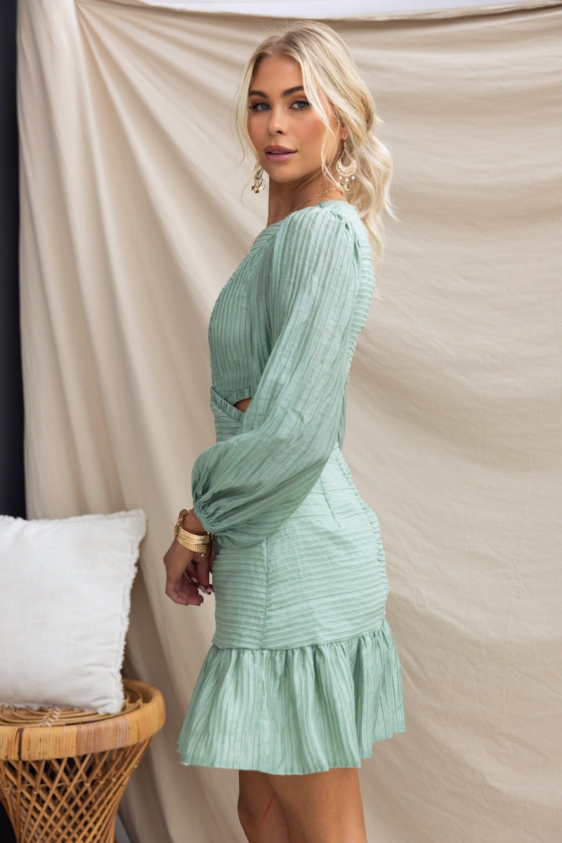 Tovia Dress in textured mint green with round neckline, cut-out waist, and ruffled hem, modeled by a woman.