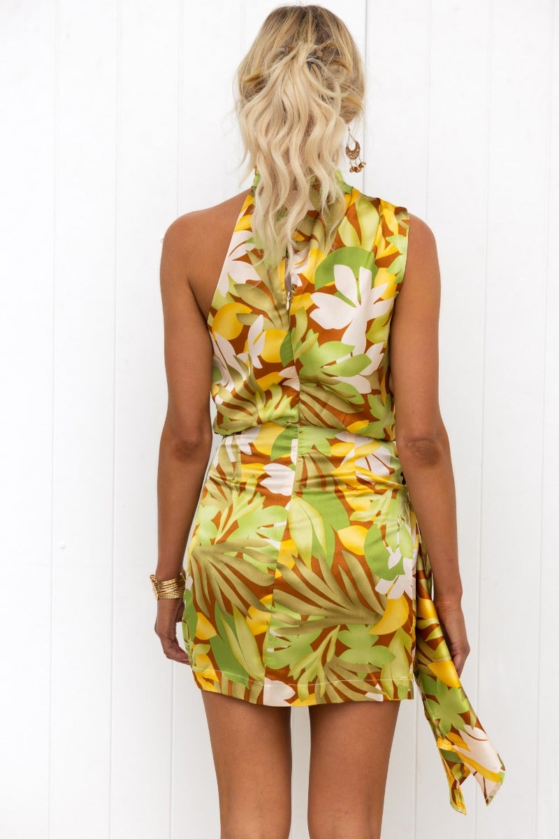 Back view of a woman in a floral satin Venus dress with a high neckline and wrap tie skirt.