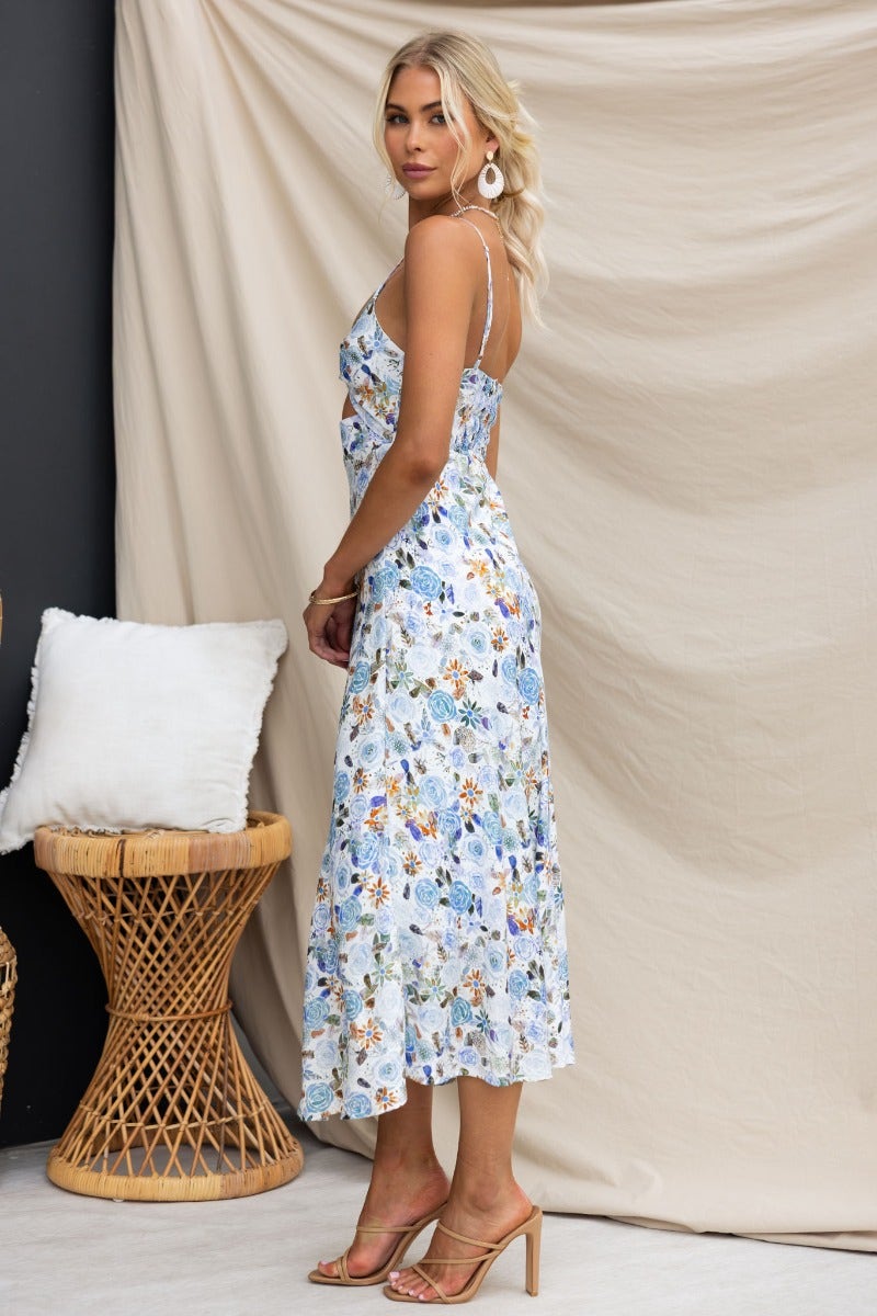 Fawn midi dress with floral print, adjustable straps, and twist detail, styled on model in summer setting.