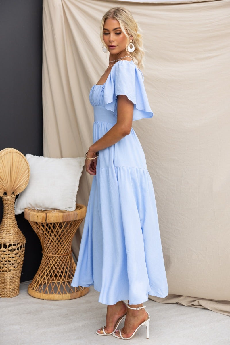 Hanni maxi dress in light blue, featuring flutter sleeves and a tie back, styled elegantly against a neutral backdrop.