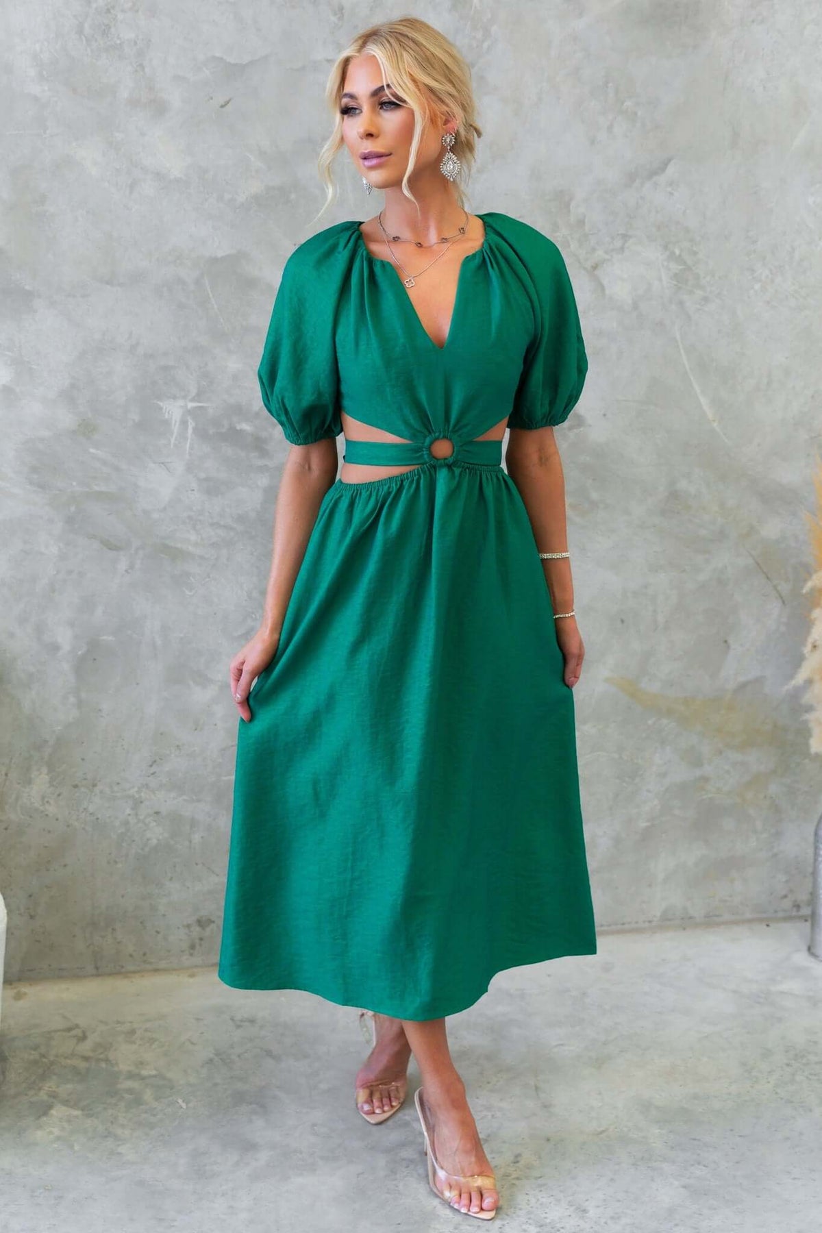 Model wearing a green midi dress with puff sleeves and cut-out waist, showcasing stylish design and elegant silhouette.