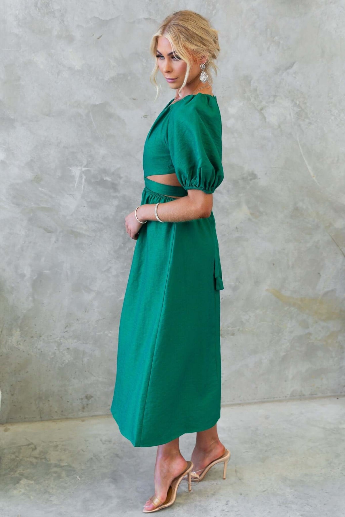 Isabelline midi dress in green with V-neckline, puff sleeves, and cut-out waist, worn by a model standing sideways.