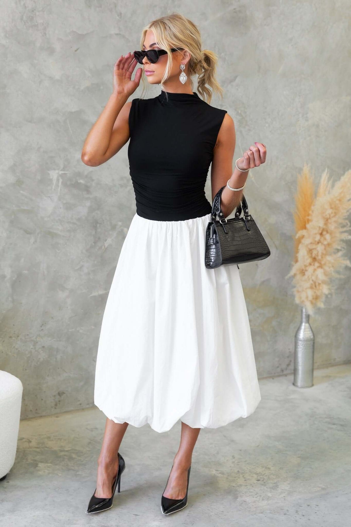 Model in black top and white Cloud Nine Midi Skirt, accessorized with sunglasses and handbag, standing against a stylish backdrop.