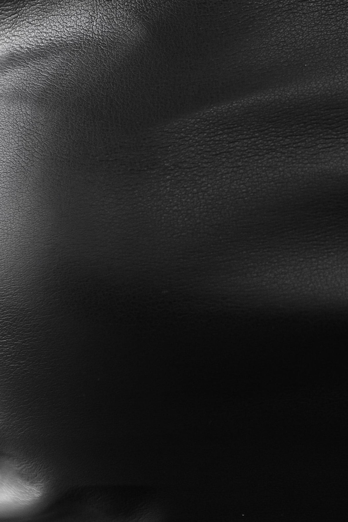 Close-up of black faux leather texture, showcasing its smooth surface and subtle grain, ideal for elegant fashion pieces.